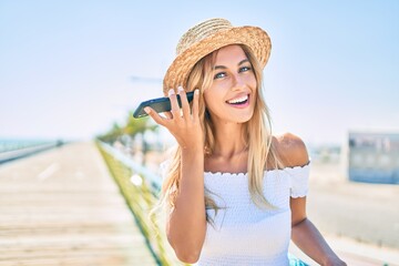 Young blonde tourist girl smiling happy listening audio message using smartphone at the promenade.