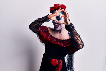 Young woman wearing mexican day of the dead makeup doing heart shape with hand and fingers smiling...