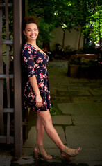 Naklejka premium Beautiful biracial woman in floral print dress poses in shaded city park - hair up