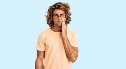 Young hispanic man wearing casual clothes and glasses touching mouth with hand with painful expression because of toothache or dental illness on teeth. dentist