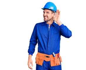 Young handsome man wearing worker uniform and hardhat smiling with hand over ear listening an hearing to rumor or gossip. deafness concept.