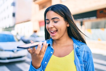 Young latin woman smiling happy sending audio message using smartphone at the city.