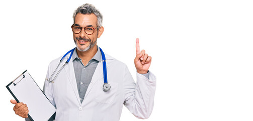 Middle age grey-haired man wearing doctor stethoscope holding clipboard surprised with an idea or...