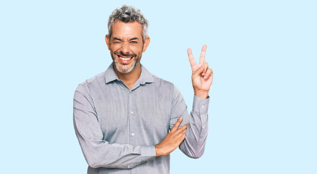 Middle age grey-haired man wearing casual clothes smiling with happy face winking at the camera doing victory sign. number two.