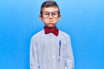 Cute blond kid wearing nerd bow tie and glasses puffing cheeks with funny face. mouth inflated with...