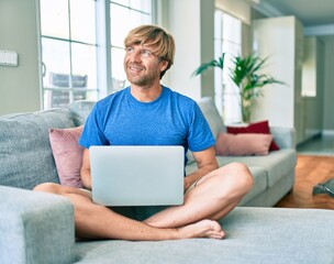 Middle age handsome caucasian man relaxing at home working with computer laptop on the sofa
