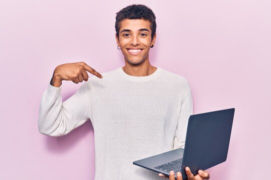 Young african amercian man holding laptop pointing finger to one self smiling happy and proud