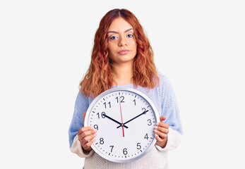 Young latin woman holding big clock thinking attitude and sober expression looking self confident