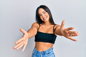 Young beautiful hispanic girl wearing casual clothes looking at the camera smiling with open arms for hug. cheerful expression embracing happiness.