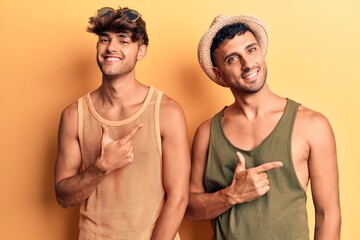 Young gay couple wearing summer clothes cheerful with a smile of face pointing with hand and finger up to the side with happy and natural expression on face