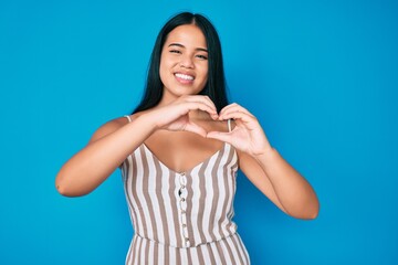 Young beautiful asian girl wearing casual clothes smiling in love doing heart symbol shape with hands. romantic concept.