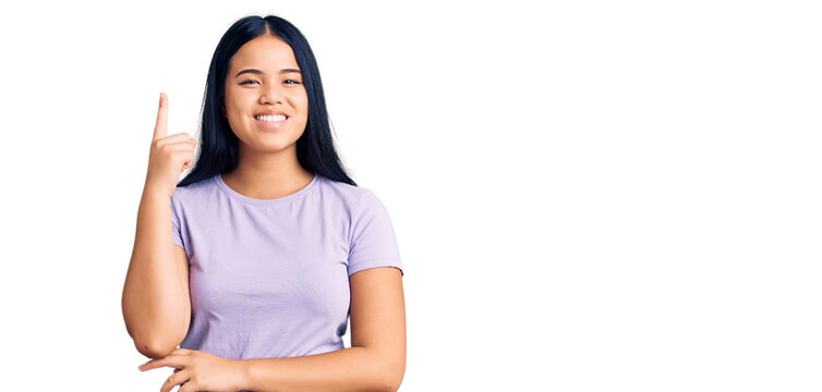 Young beautiful asian girl wearing casual clothes pointing finger up with successful idea. exited and happy. number one.