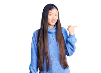 Young beautiful chinese woman wearing casual turtleneck sweater smiling with happy face looking and pointing to the side with thumb up.