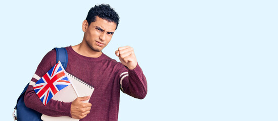 Hispanic handsome young man exchange student holding uk flag annoyed and frustrated shouting with anger, yelling crazy with anger and hand raised