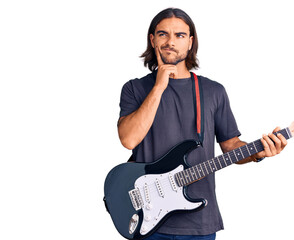 Young handsome man playing electric guitar serious face thinking about question with hand on chin,...