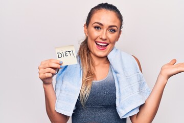 Young beautiful blonde sporty woman using towel holding diet reminder over white background celebrating achievement with happy smile and winner expression with raised hand