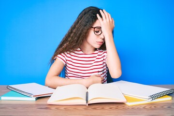 Cute hispanic child girl studying for school exam sitting on the table surprised with hand on head for mistake, remember error. forgot, bad memory concept.