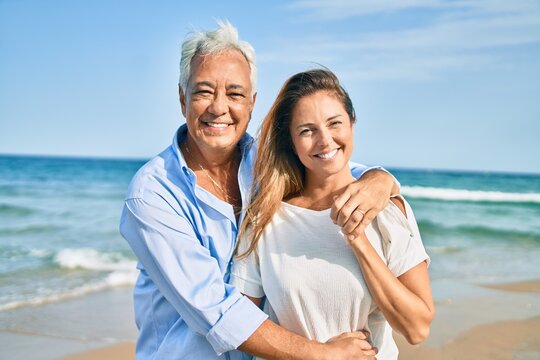 Middle Age Hispanic Couple Smiling Happy And Hugging Walking At The Beach