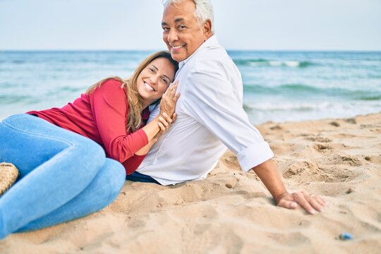 Middle age hispanic couple smiling happy and hugging sitting at the beach