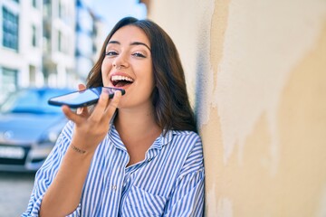 Fototapeta premium Young hispanic businesswoman smiling happy sending voice message using smartphone at the city.