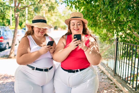 Two plus size overweight sisters twins women with smartphone outdoors on a sunny day