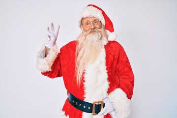 Old senior man with grey hair and long beard wearing santa claus costume with suspenders showing and pointing up with fingers number three while smiling confident and happy.