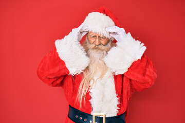 Old senior man with grey hair and long beard wearing traditional santa claus costume with hand on head for pain in head because stress. suffering migraine.