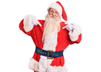 Old senior man with grey hair and long beard wearing traditional santa claus costume looking confident with smile on face, pointing oneself with fingers proud and happy.