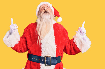 Old senior man with grey hair and long beard wearing traditional santa claus costume amazed and...