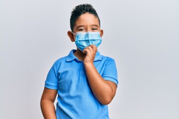 Little boy hispanic kid wearing medical mask smiling looking confident at the camera with crossed...
