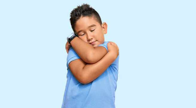 Little Boy Hispanic Kid Wearing Casual Clothes Hugging Oneself Happy And Positive, Smiling Confident. Self Love And Self Care