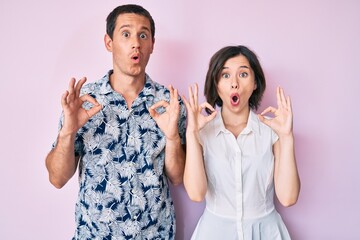 Beautiful couple wearing casual clothes looking surprised and shocked doing ok approval symbol with fingers. crazy expression