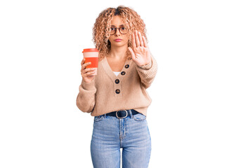 Young blonde woman with curly hair wearing glasses and drinking a cup of coffee with open hand doing stop sign with serious and confident expression, defense gesture