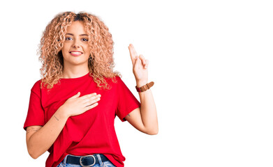 Young blonde woman with curly hair wearing casual red tshirt smiling swearing with hand on chest...