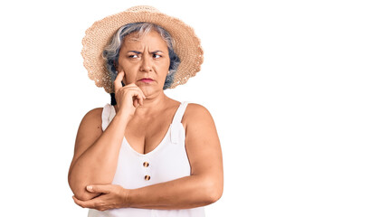 Senior woman with gray hair wearing summer hat and summer clothes serious face thinking about question with hand on chin, thoughtful about confusing idea