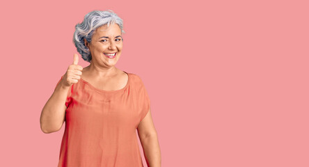 Senior woman with gray hair wearing orange tshirt smiling happy and positive, thumb up doing excellent and approval sign
