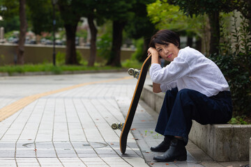 スケートボードを持ち休憩する50代の女性