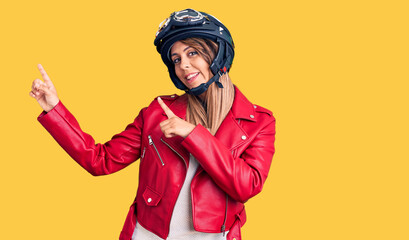 Young beautiful woman wearing motorcycle helmet smiling and looking at the camera pointing with two hands and fingers to the side.