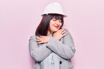 Naklejka premium Young plus size woman wearing architect hardhat hugging oneself happy and positive, smiling confident. self love and self care