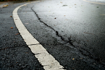 Close up to bur of asphalt road with white line. Float the cracked road and the glare of the wet...