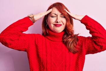 Young beautiful redhead woman wearing red casual turtleneck sweater over pink background with hand on head, headache because stress. Suffering migraine.
