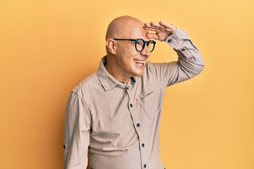 Fototapeta premium Middle age bald man wearing casual clothes and glasses very happy and smiling looking far away with hand over head. searching concept.