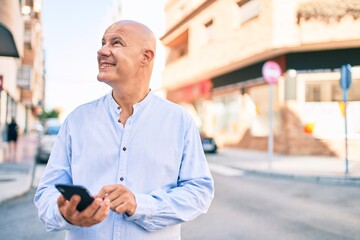 Middle age bald man smiling happy using smartphone at the city.