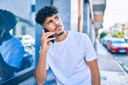 Young arab man with serious expression talking on the smartphone leaning on the wall.