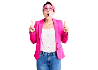 Obraz na płótnie Canvas Young beautiful woman with pink hair wearing business jacket and glasses amazed and surprised looking up and pointing with fingers and raised arms.