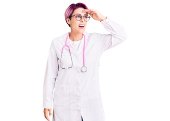 Young beautiful woman with pink hair wearing doctor uniform very happy and smiling looking far away with hand over head. searching concept.