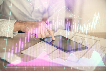 Double exposure of man's hands holding and using a digital device and forex graph drawing. Financial market concept.