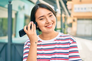 Young latin girl smiling happy listening audio message using smartphone at the city