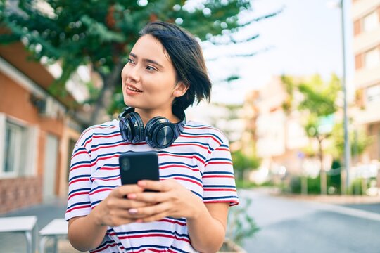 Young latin girl smiling happy using smartphone and headphones at the city