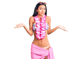Young beautiful latin girl wearing bikini and hawaiian lei clueless and confused expression with...